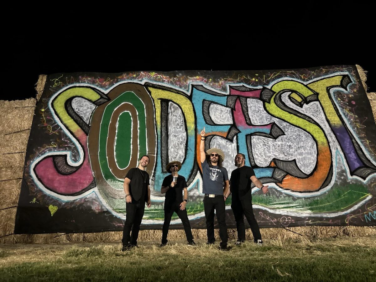 The four members of Patrick & the LVB standing together at night in front of a giant hand-painted SODFEST mural on stacked hay bales, Patrick center with his fist raised.